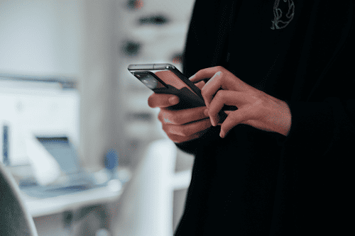 A person in a black outfit is using a smartphone with both hands.
